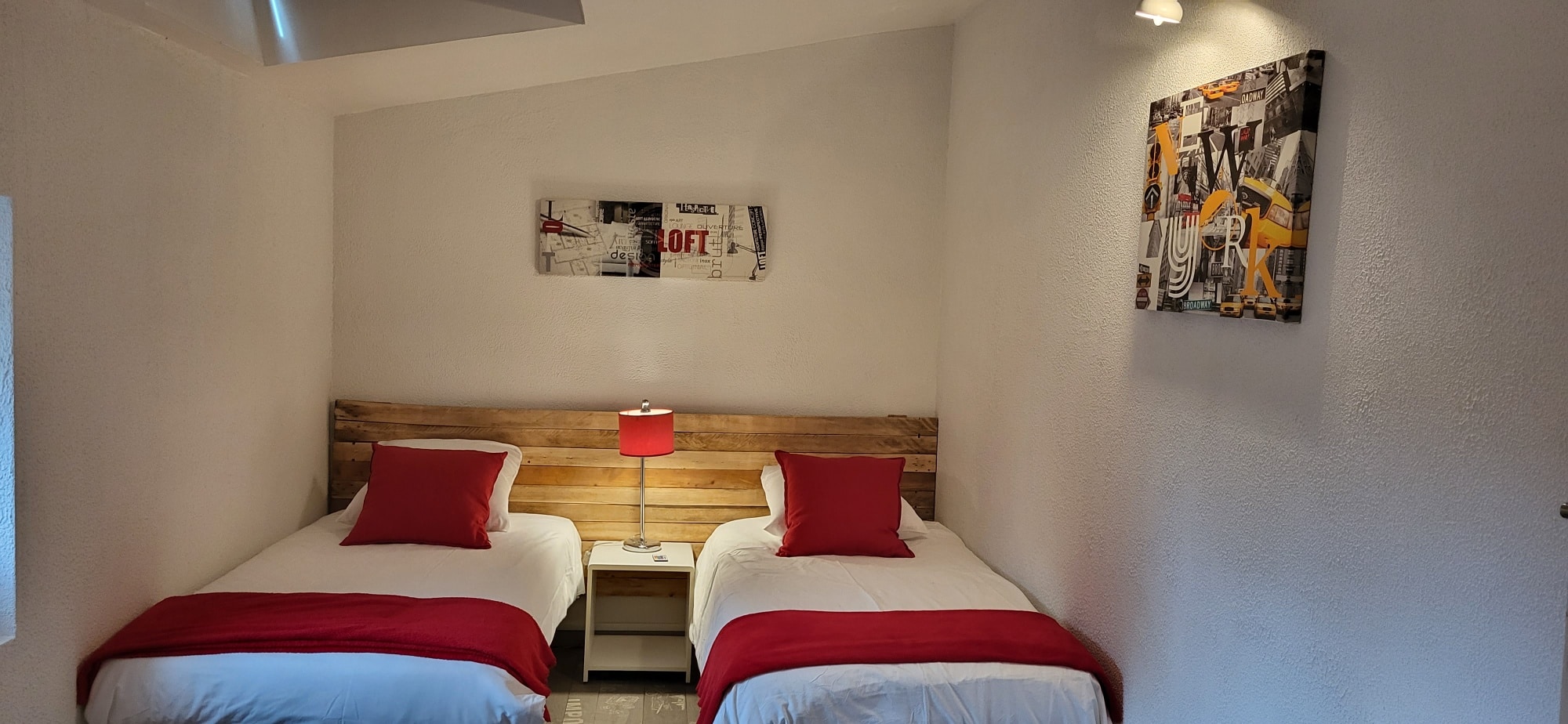 Chambre double moderne avec deux lits simples. Tête de lit en bois, lampe rouge. Décorations murales "LOFT" et collage "NEW YORK".