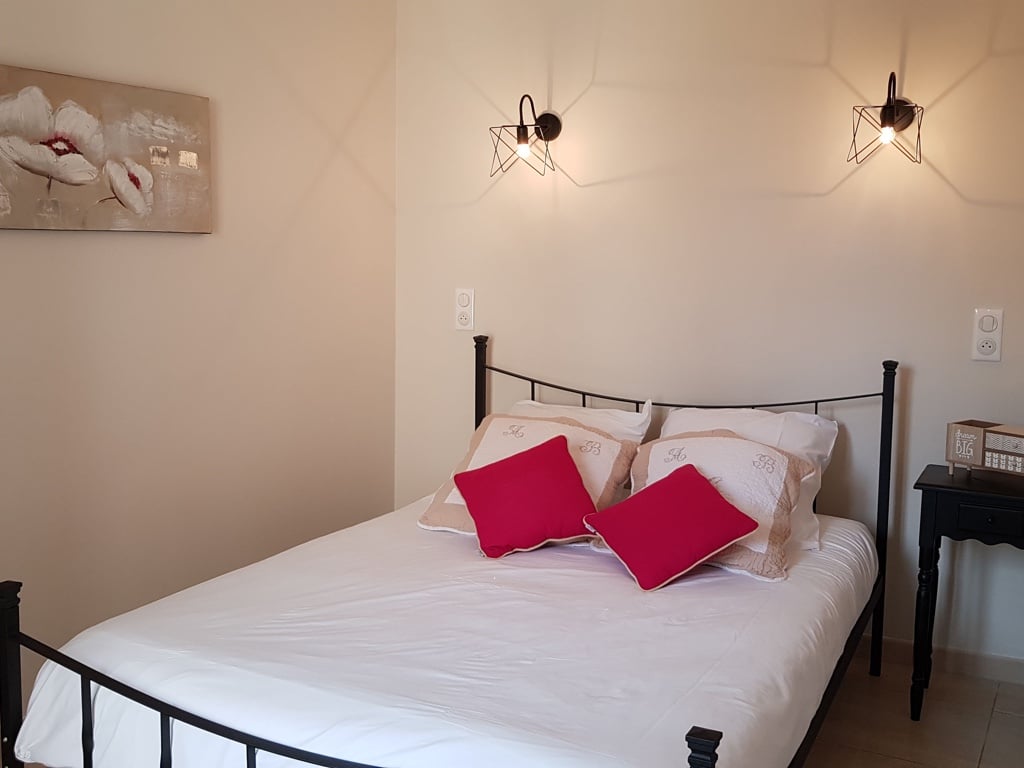 Lit double en fer forgé dans une chambre cozy. Coussins rouges, art floral mural et appliques industrielles. Boîte de chevet affichant "dream BIG".