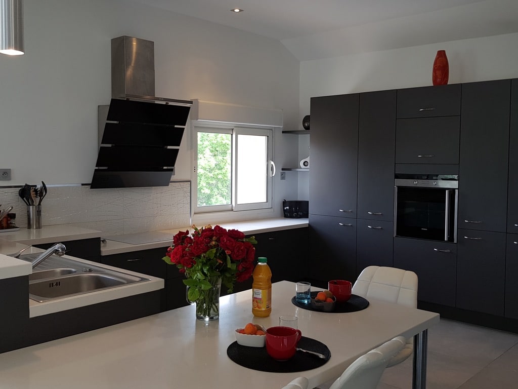Cuisine moderne design, armoires gris anthracite, îlot blanc. Hotte inclinée noire, four encastré, roses rouges.