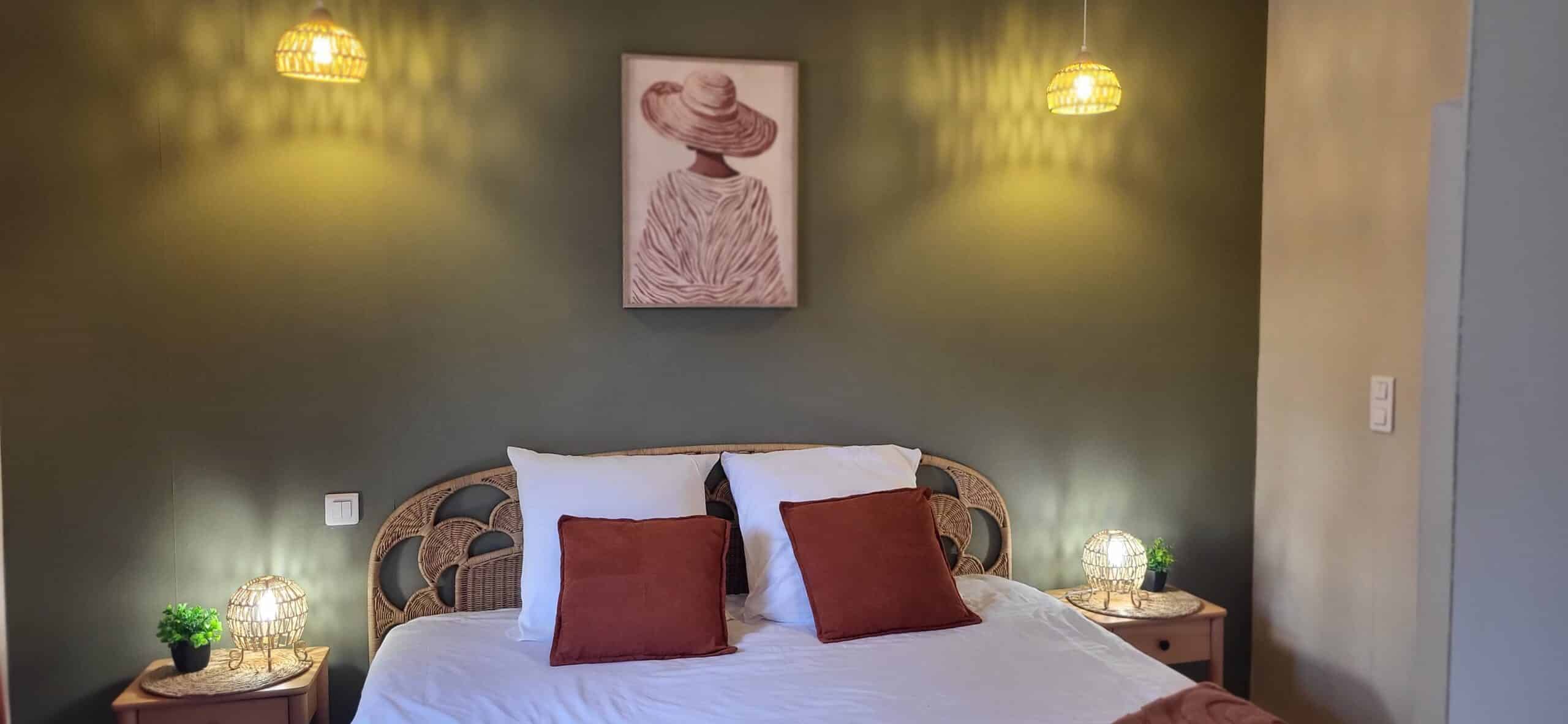 Chambre bohème avec mur vert olive, tête de lit en rotin, coussins terre cuite et luminaires chaleureux en osier.