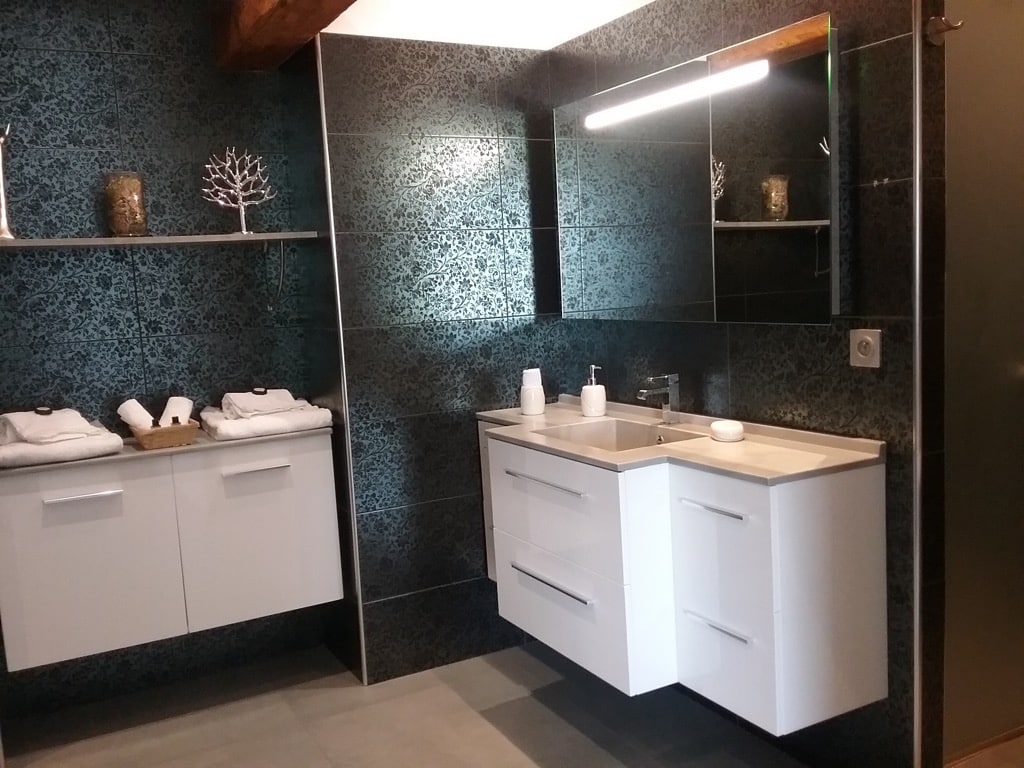 Meubles-vasques blancs suspendus dans une salle de bain moderne. Le carrelage mural sombre présente un motif floral riche.