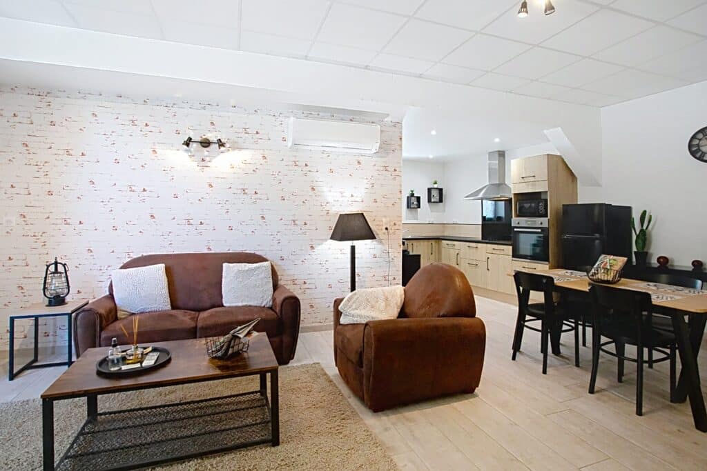 Salon Moderne et Cuisine Ouverte : Déco Industrielle Chic Salon chaleureux avec canapé marron, mur effet briques blanches et cuisine ouverte moderne aménagée.