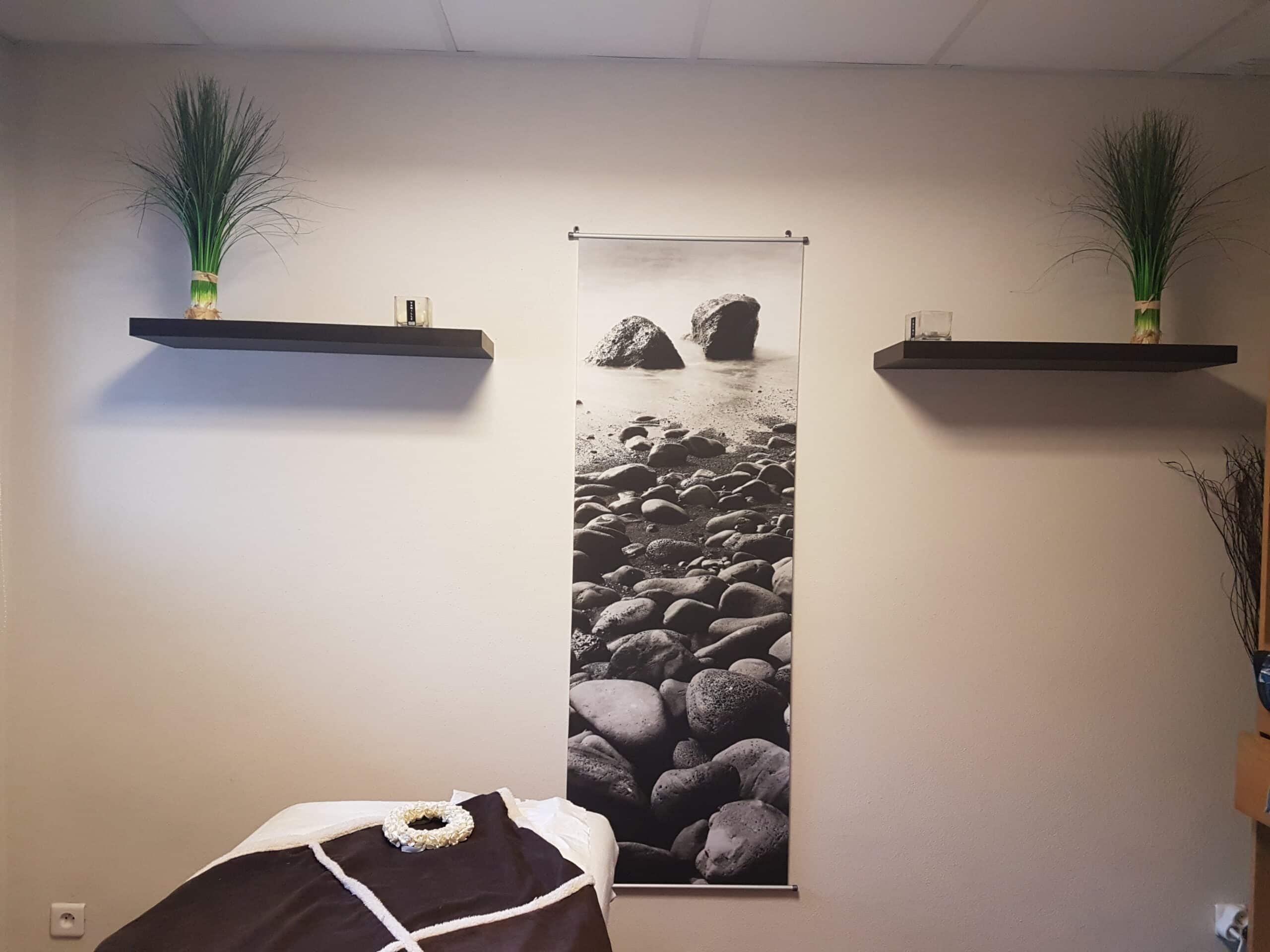Décoration zen de salle de massage avec poster de plage de galets, étagères flottantes et plantes vertes apaisantes.