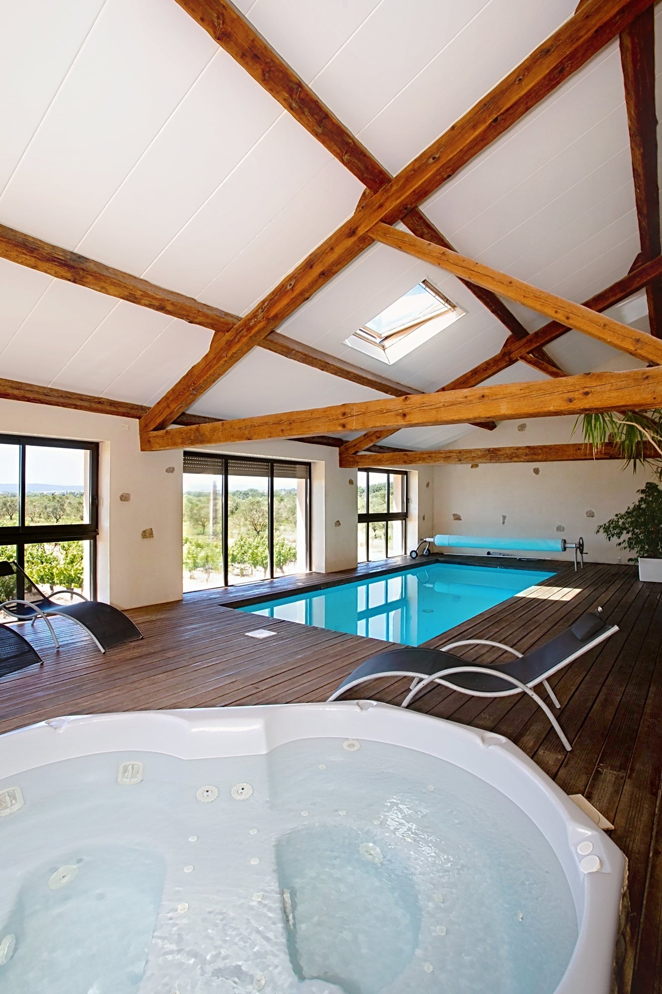 Espace spa avec piscine intérieure, jacuzzi et poutres bois offrant une vue relaxante sur la nature environnante.