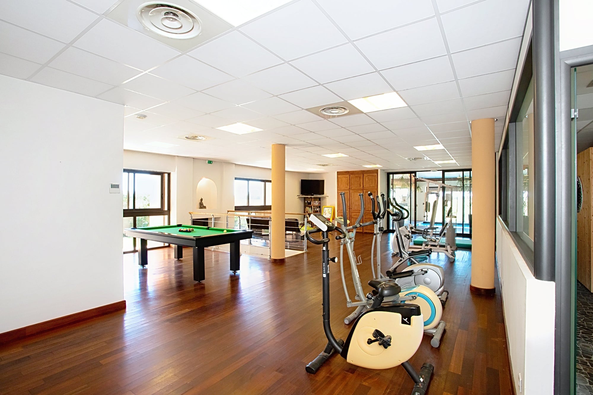 Salle de sport et loisirs avec table de billard, vélos elliptiques et appareils de fitness sur parquet.