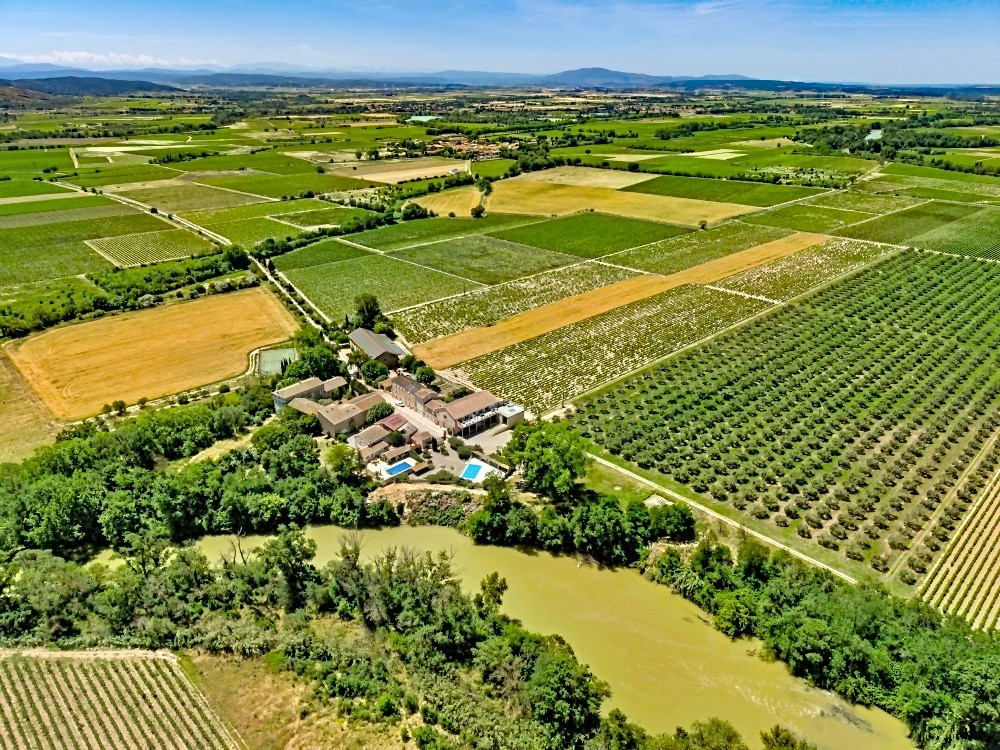 Vue aérienne d'un domaine viticole avec piscines bordant une rivière au cœur de champs agricoles et vignobles.